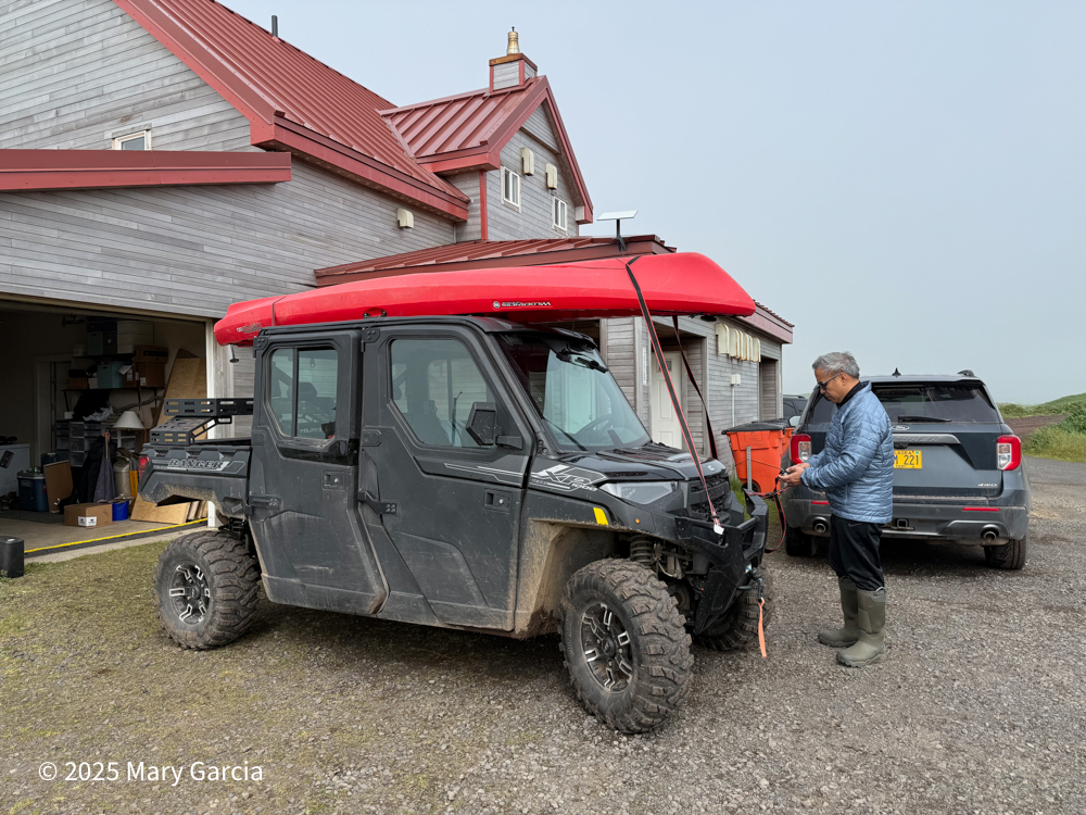 Carlos securing a red kayak to the top of the Polaris before a paddle on St. Paul Island