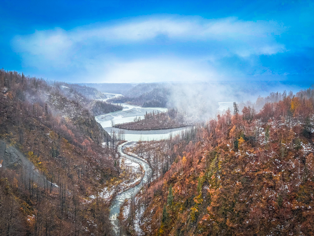 Aerial view of the winding Chulitna River surrounded by autumn forest and mist in Denali National Park, Alaska.