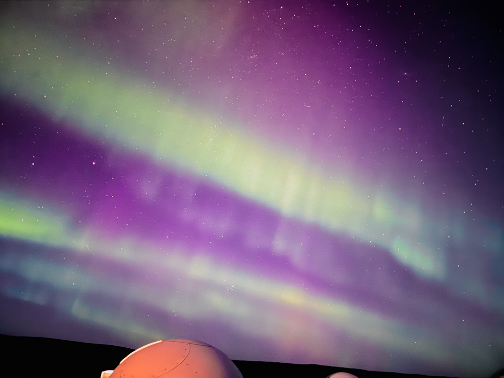 Vibrant green and purple Northern Lights shining over a dome-shaped cabin at Aurora Borealis Basecamp near Fairbanks, Alaska.