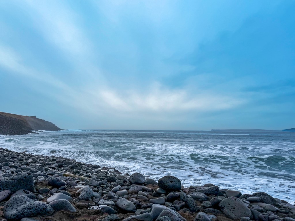Rocky shoreline and waves of the Bering Sea under a wide blue sky at St. Paul Island, Alaska
