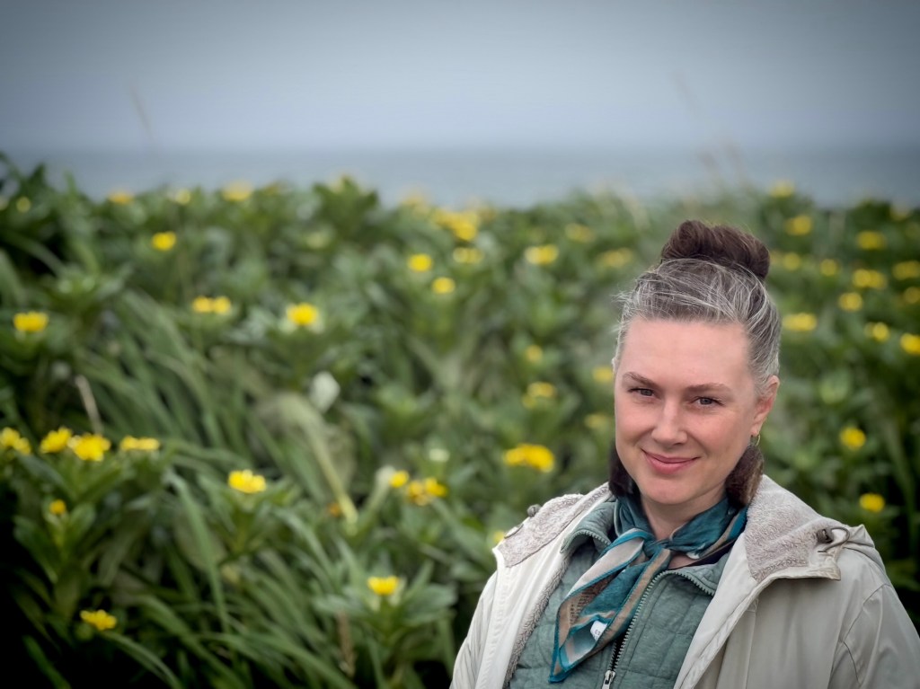 Woman standing among yellow summer beach flowers near the Bering Sea on St. Paul Island, Alaska.